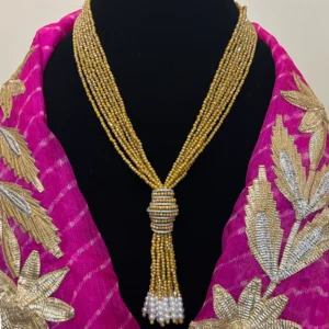Beige Long Necklace in Crystal Beads Tassel Style displayed on a black stand making a v neck with a magenta saree