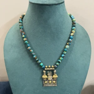 Close-up of a handcrafted tribal peacock pendant necklace featuring an oxidized pendant and turquoise mottled beads on a green bust display